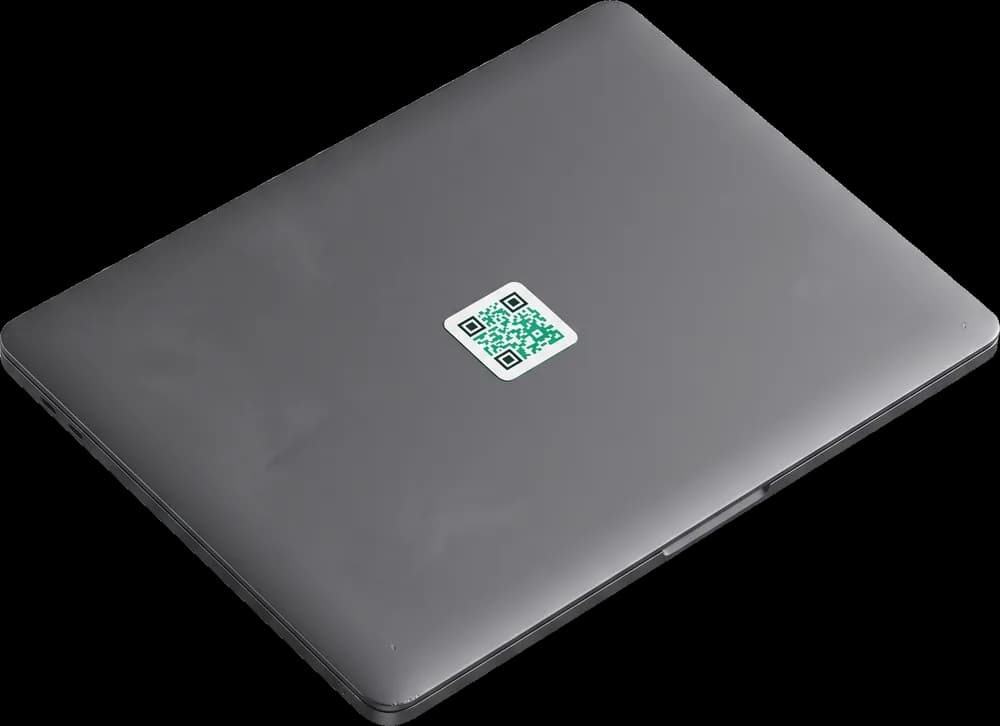 Open laptop tagged with an emerald QR asset tag below the trackpad